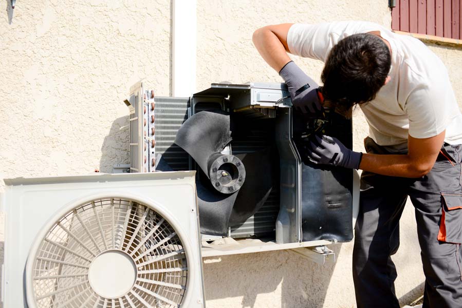 young man electrician installer working on outdoor compressor unit air conditioner at a client's home.