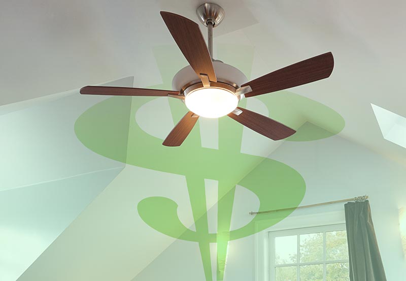 A modern five-blade wooden ceiling fan with a warm, illuminated central light fixture, mounted to a bright white ceiling inside a room.