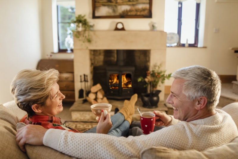 couple sat in front of a fire drinking hot chocolate from mugs.